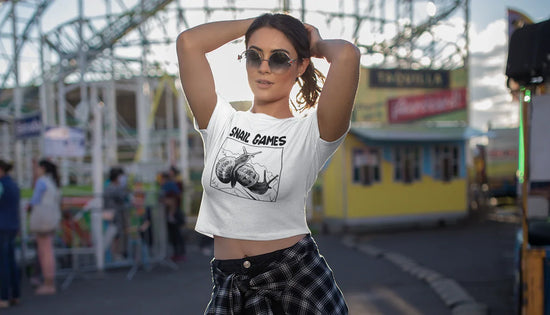 Woman in white crop top with 'SNAIL GAMES' graphic, standing at outdoor fairground