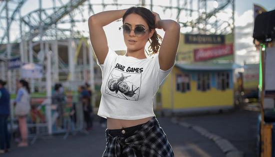 Woman in white crop top with 'SNAIL GAMES' graphic, standing at outdoor fairground